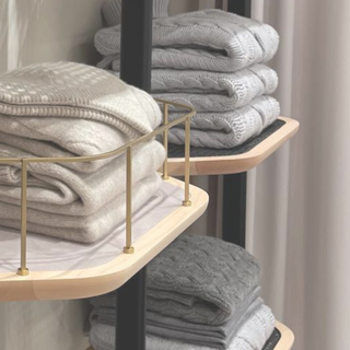 Stacked neutral-tone cashmere sweaters displayed on wooden shelves with brass details inside Assoluto boutique in Rome