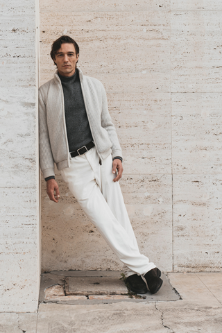 Man wearing grey wool cardigan by Fedeli with dark turtleneck and white trousers — Italian menswear available at Assoluto Studio.